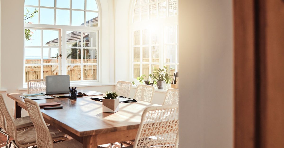 A luxury dining room features large curved multi-pane windows with intense sunlight shining through into the space.