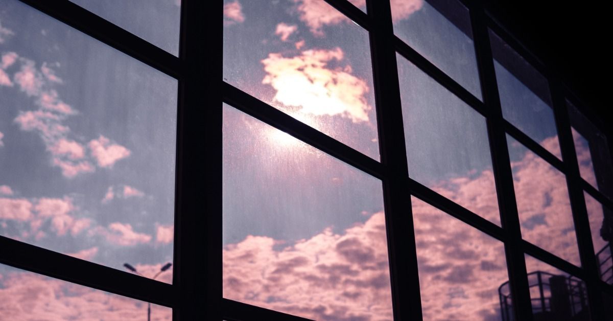 Sunlight shining through large window panes with a grid frame, illuminating clouds with soft pink.