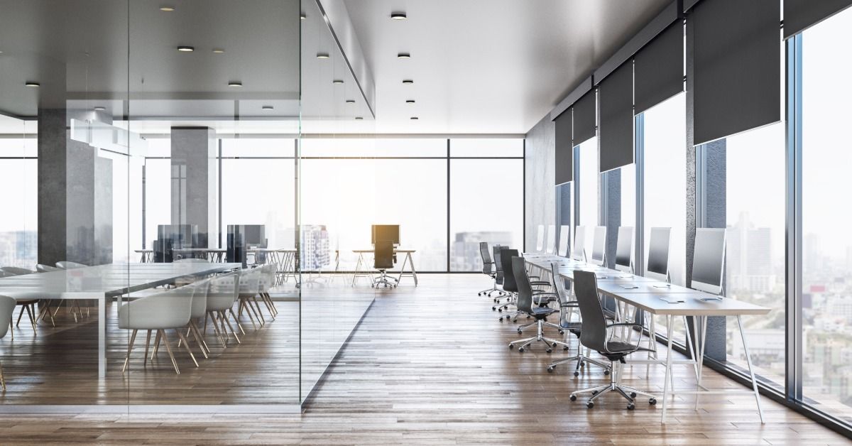 A modern office with a glass-walled meeting room, computer workstations, and floor-to-ceiling window