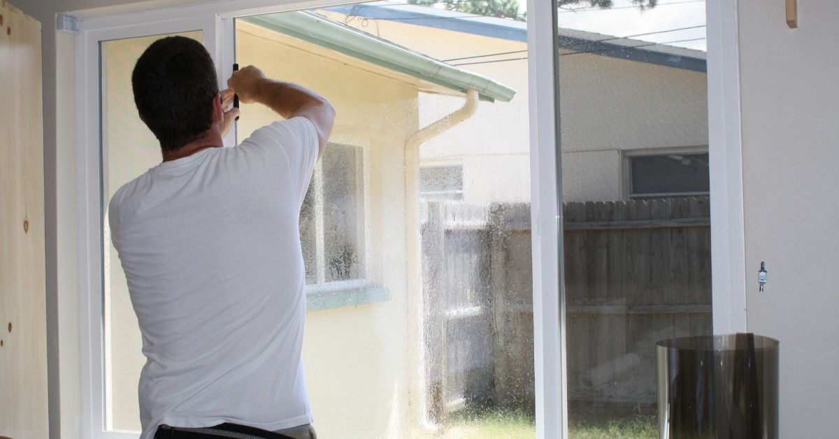 A technician installs window film on a large sliding glass door, smoothing the surface during applic