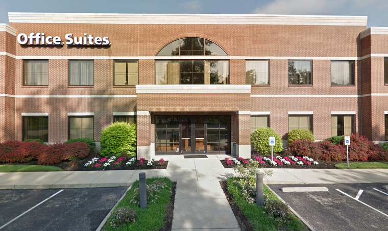 Brick office building with “Office Suites” sign, central entrance, and landscaped parking lot