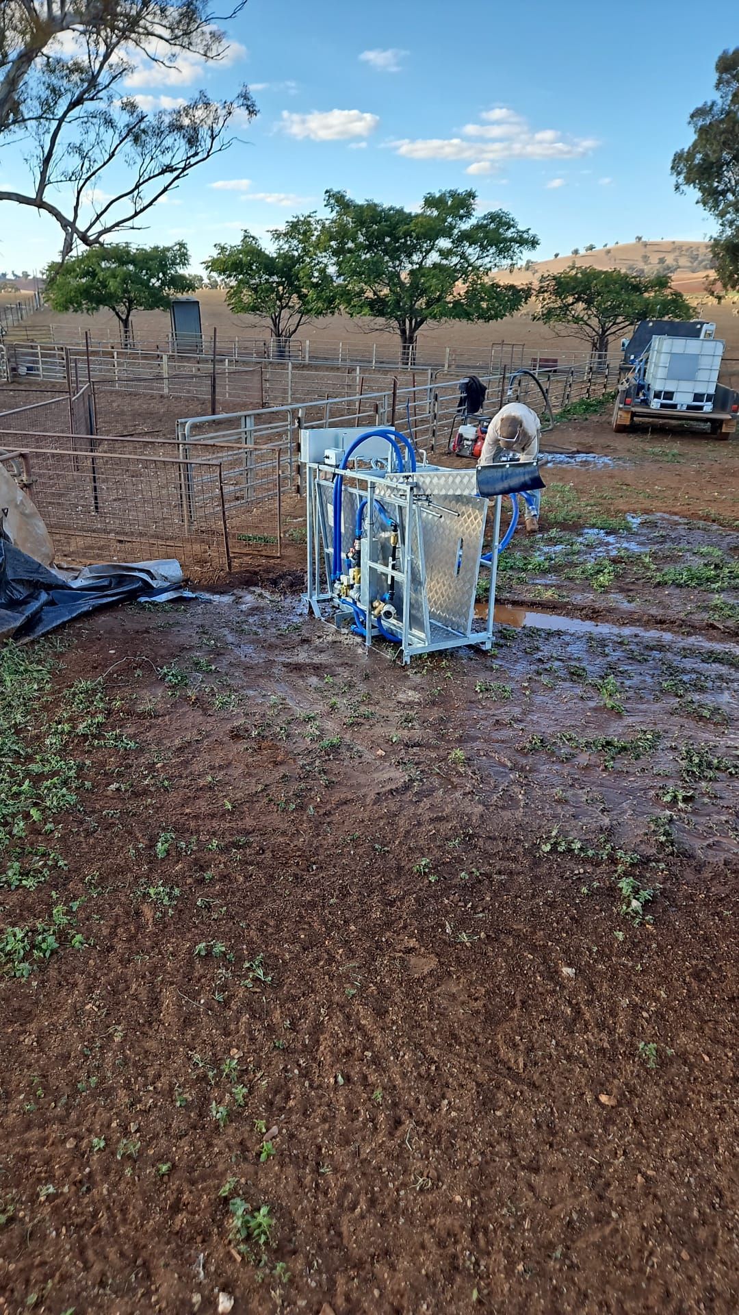 Worker operating a blue metal machine beside a brick wall in a muddy outdoor yard under a cloudy sky — Dusty Rural Contracting in Coolac, NSW