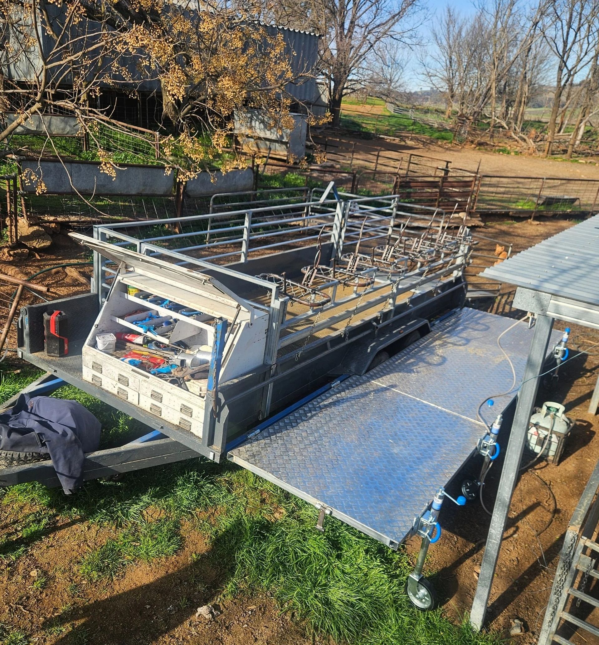 Large flatbed trailer with metal railings and a blue tarp in a rural yard — Dusty Rural Contracting in Coolac, NSW