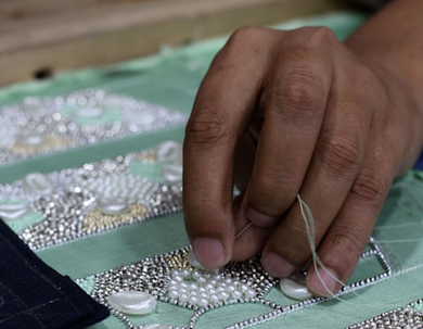Gros plan sur des mains cousant des perles blanches sur un tissu vert