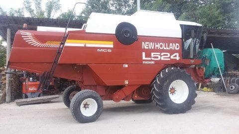 Mietitrebbia New Holland L524 arancione parcheggiata all'aperto con un accessorio verde.