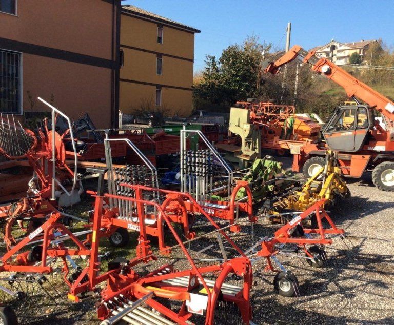 Macchinari agricoli e trattori rossi parcheggiati in un piazzale di ghiaia accanto a un edificio