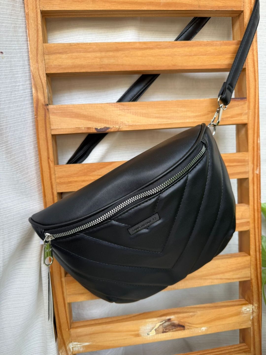 Bolso bandolera de piel negra con ojales plateados colgado de una estantería de madera con forma de escalera.
