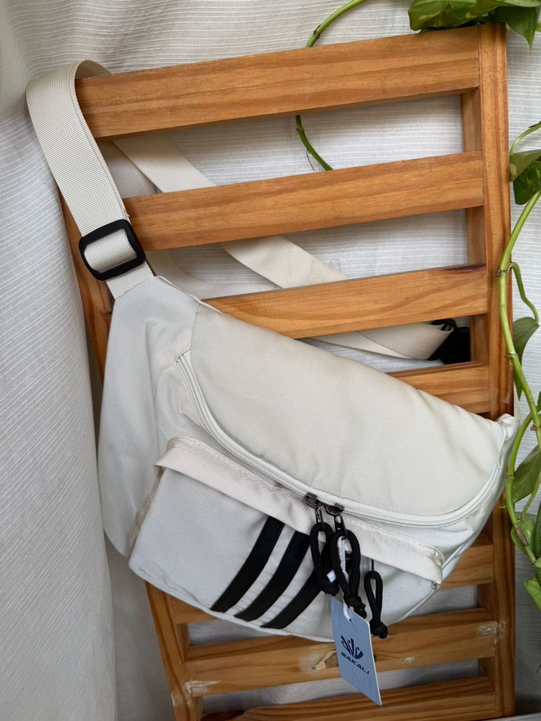 Bolso bandolera blanco con rayas negras colgado de una estantería de madera.
