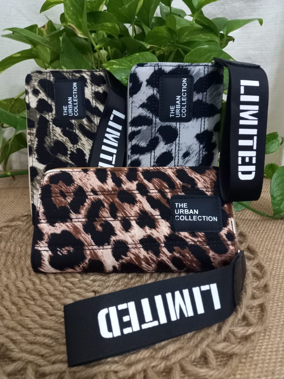 Bolso con estampado de leopardo y correas negras con el texto “LIMITED” sobre una estera tejida junto a una planta verde.