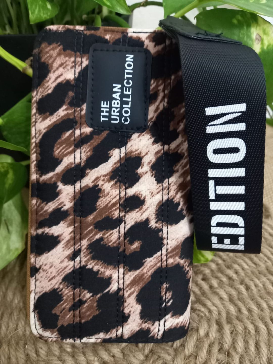 Bolso con estampado de leopardo y correas negras con el texto “LIMITED” sobre una estera tejida junto a una planta verde.
