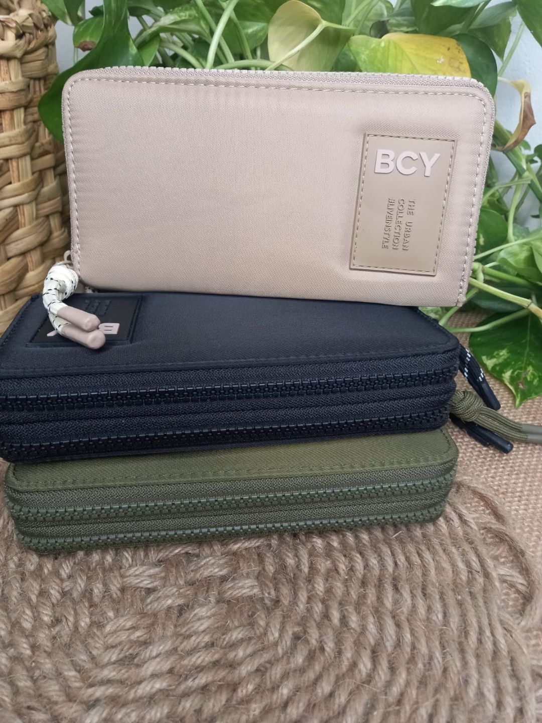 Tres estuches con cremallera de la marca BCY en color beige, azul marino y verde oliva sobre un fondo con estampado de hojas.