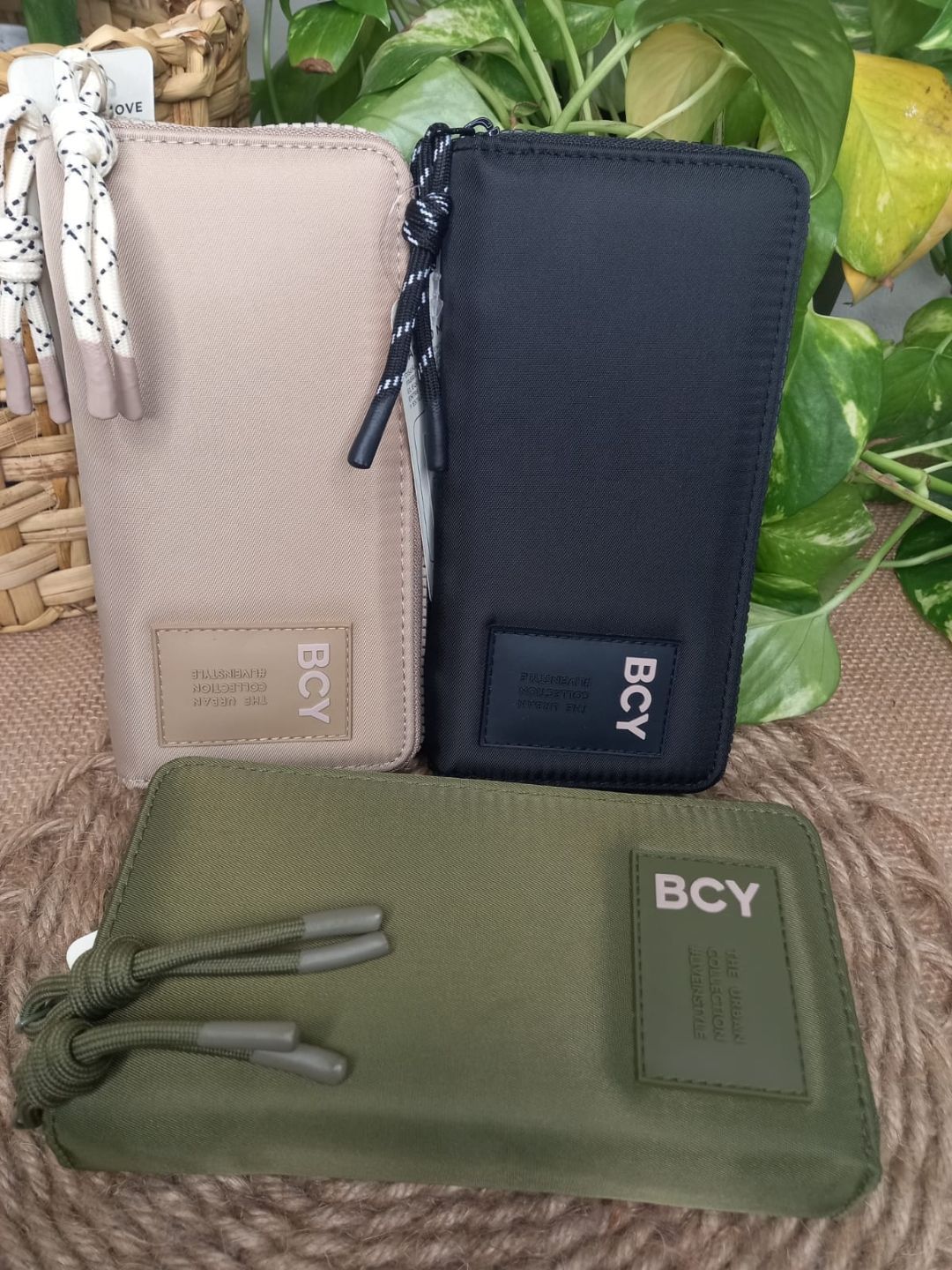 Tres estuches con cremallera de la marca BCY en color beige, azul marino y verde oliva sobre un fondo con estampado de hojas.