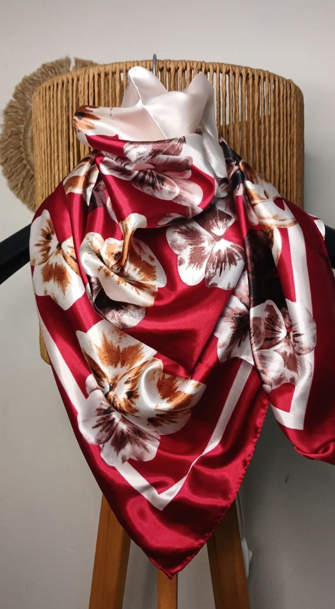 Bufanda de satén roja con estampado floral drapeada sobre un busto de maniquí tejido contra una pared de color neutro.