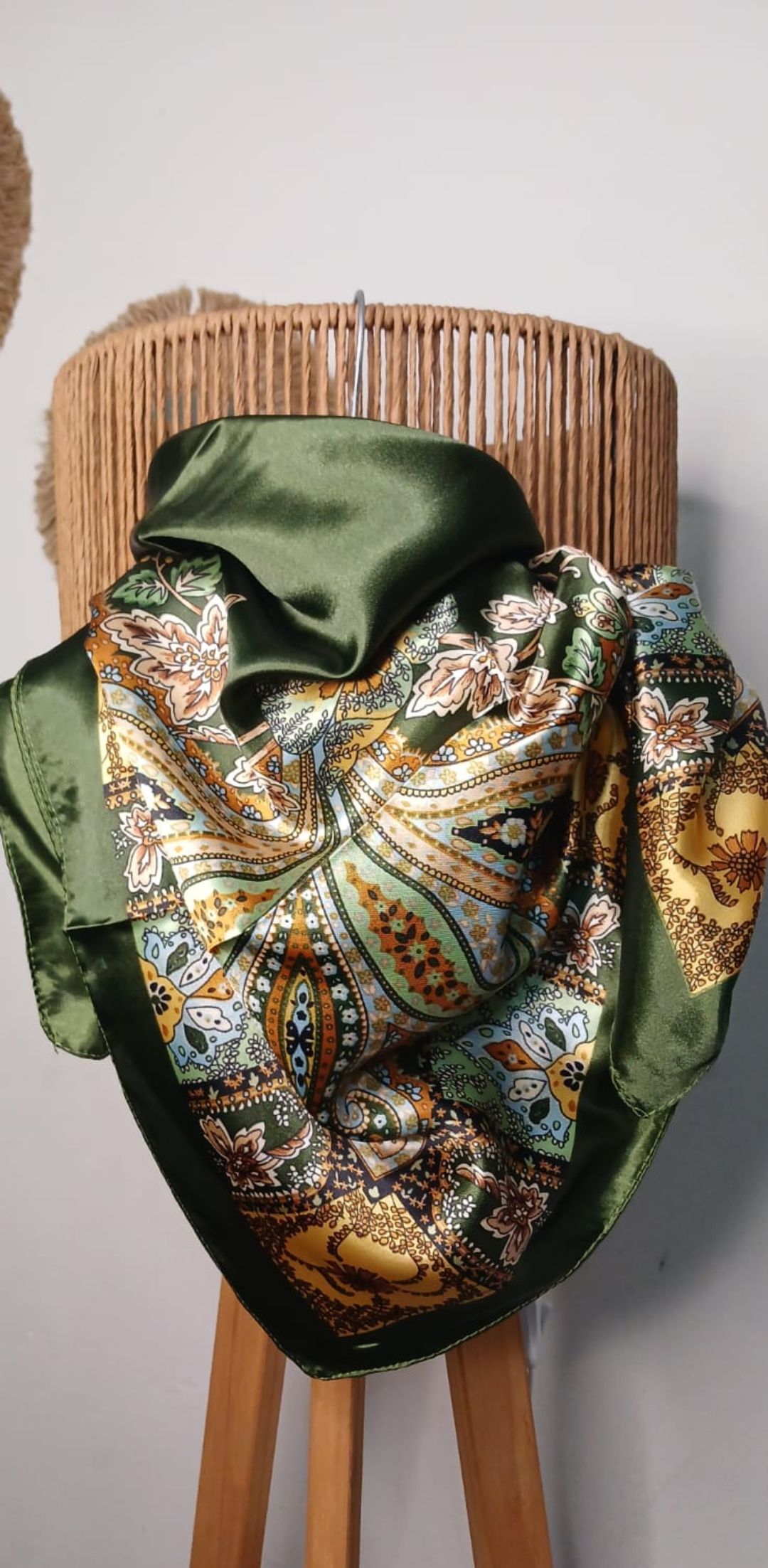 Bufanda de satén roja con estampado floral drapeada sobre un busto de maniquí tejido contra una pared de color neutro.