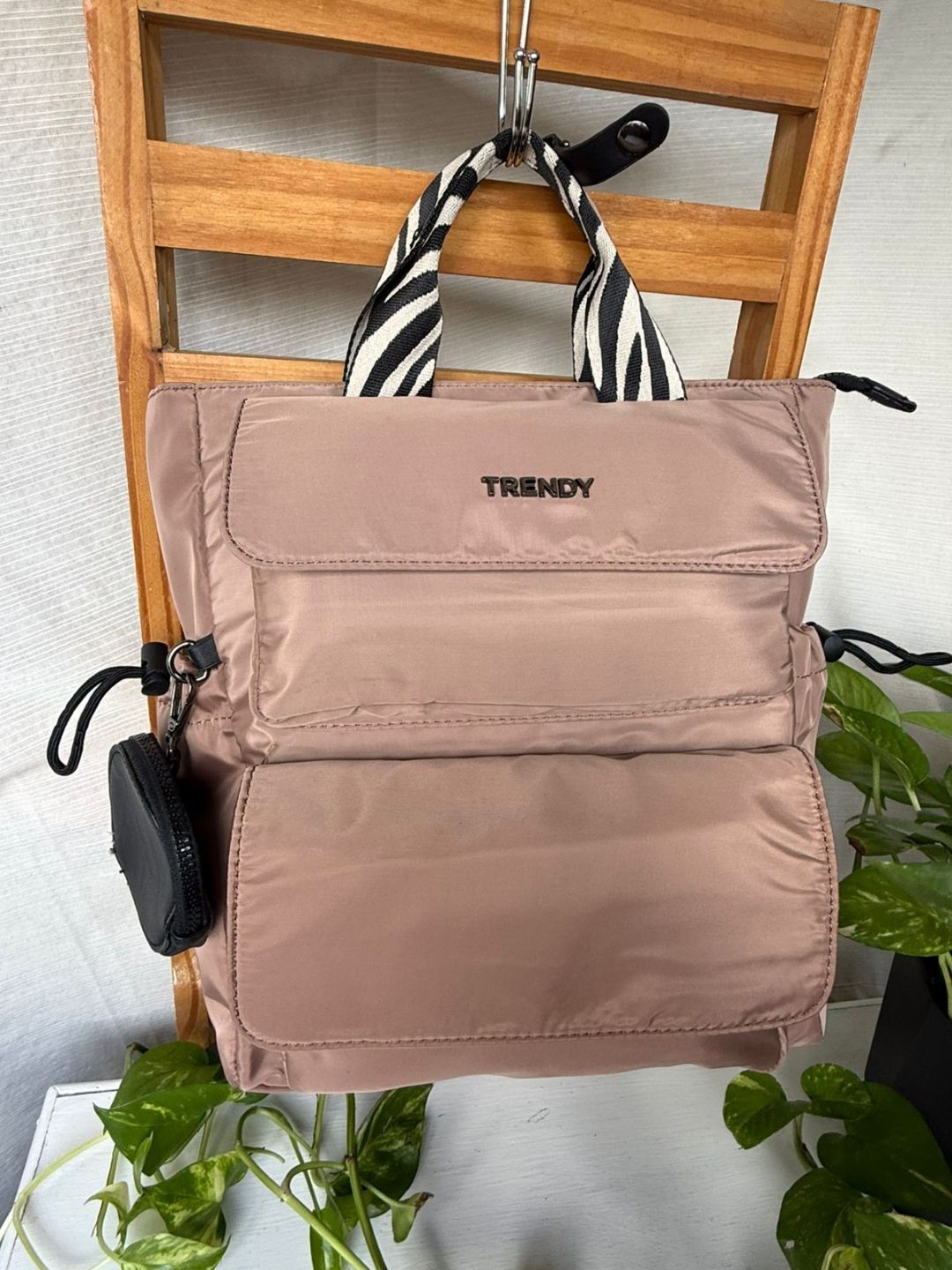 Mochila gris colgada de una silla de madera con una correa a rayas blancas y negras y un pequeño bolsillo lateral.