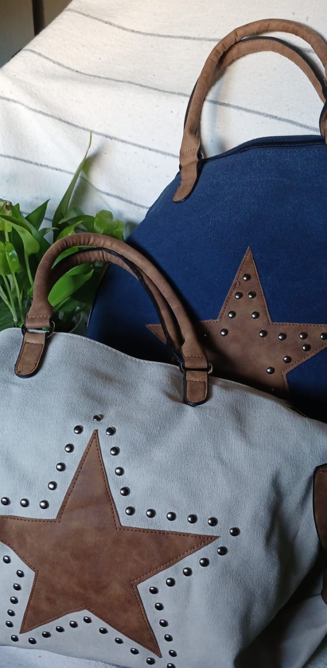 Dos bolsos de mano con estampado de estrellas, uno gris y otro azul, con asas color camel y apliques de estrellas marrones.