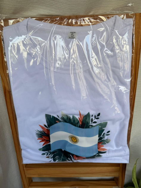 Camiseta blanca doblada en envase de plástico transparente con un gráfico de la bandera argentina en la parte delantera.