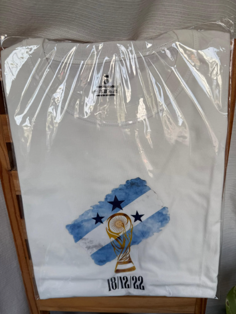 Camiseta blanca doblada en envase de plástico transparente con un gráfico de la bandera argentina en la parte delantera.