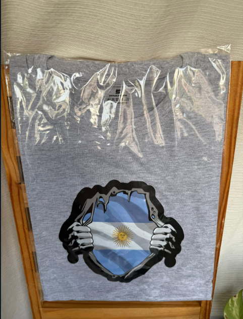Camiseta azul claro con un dibujo de una esposas rotas alrededor de una bandera argentina.