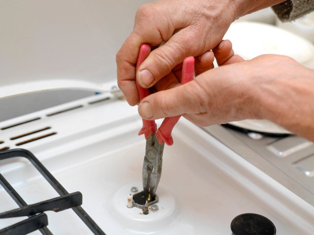 Man Repairing A Gas Stove With Pliers — Plumbers & Gasfitters in the Darling Downs