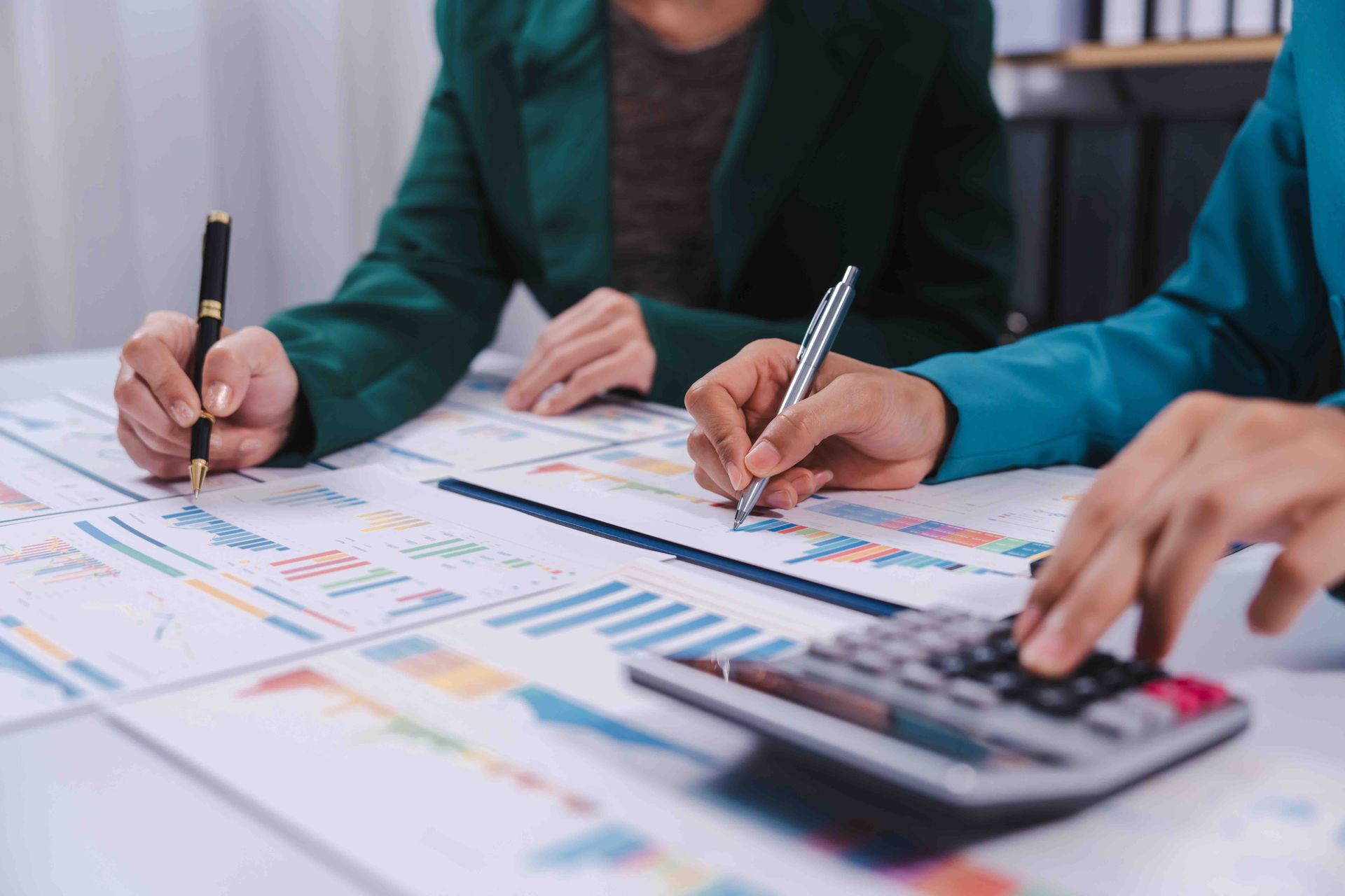 Two people are sitting at a table with a calculator and a pen.