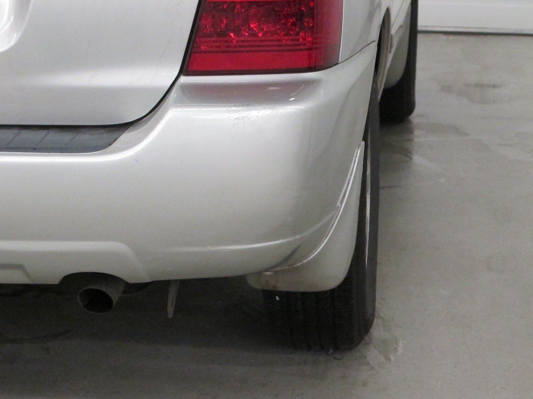 A silver car with a red tail light is parked in a garage