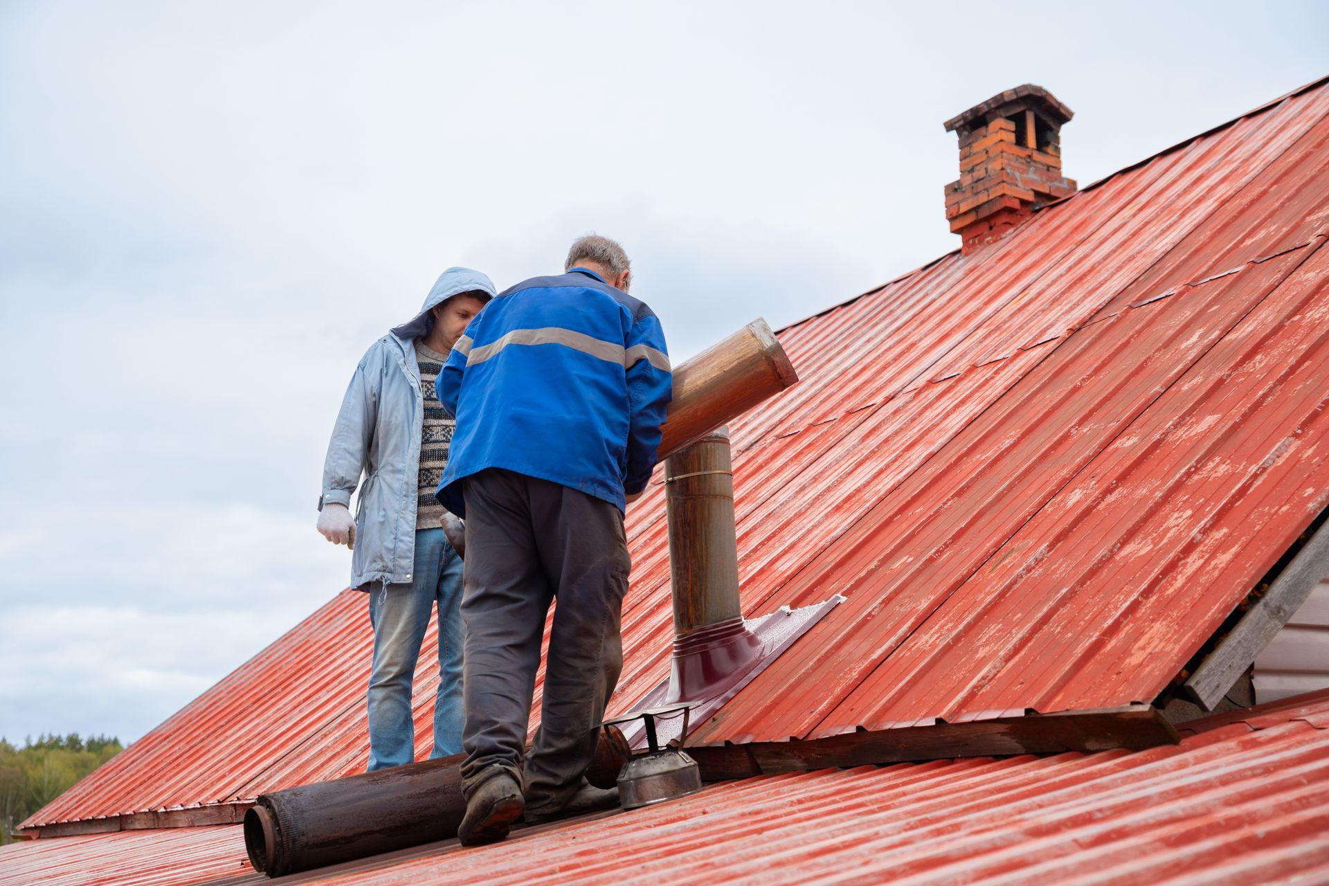 Two workers on a red metal roof installing a chimney flashing Two workers repairing a red metal roof on a house