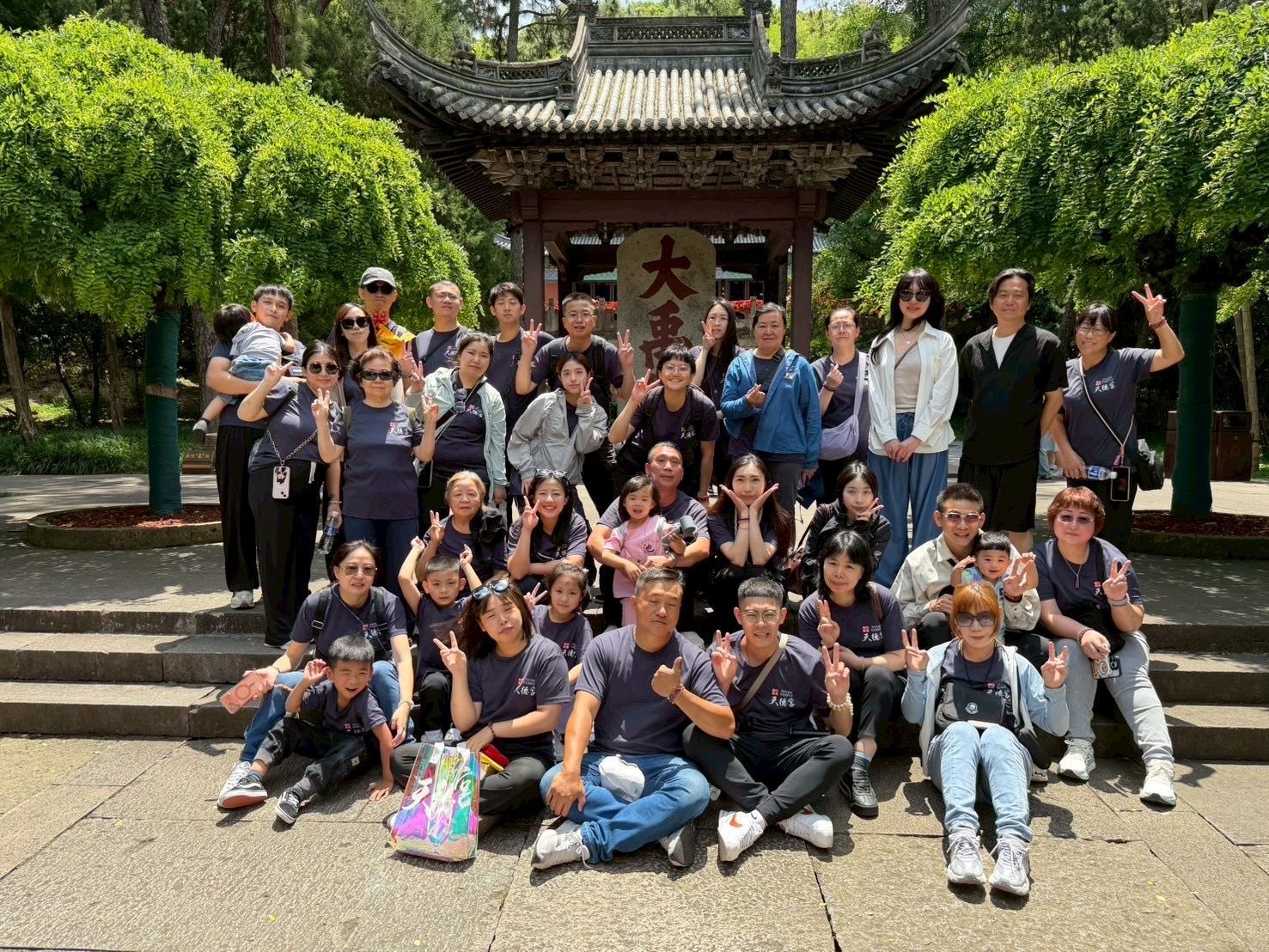 一大群人在一座傳統寺廟大門前合影，大門周圍綠藤纏繞，石階林立。