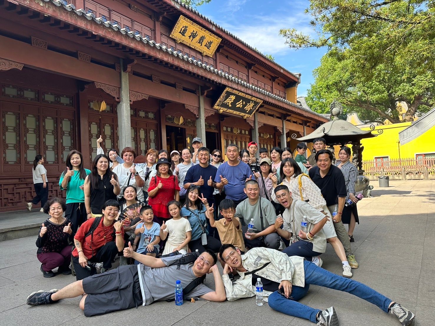 一大群人在一座傳統木屋前合影，幾個人躺在前面，其他人站在後面。