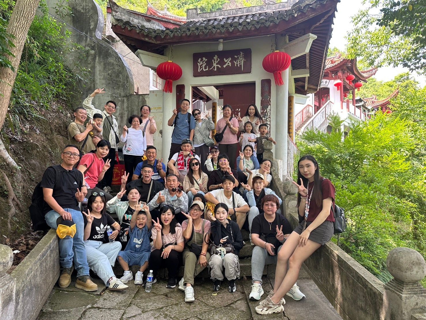 一大群人在寺廟階梯上合影，寺廟入口處是紅瓦屋頂，懸掛著燈籠和中文招牌。