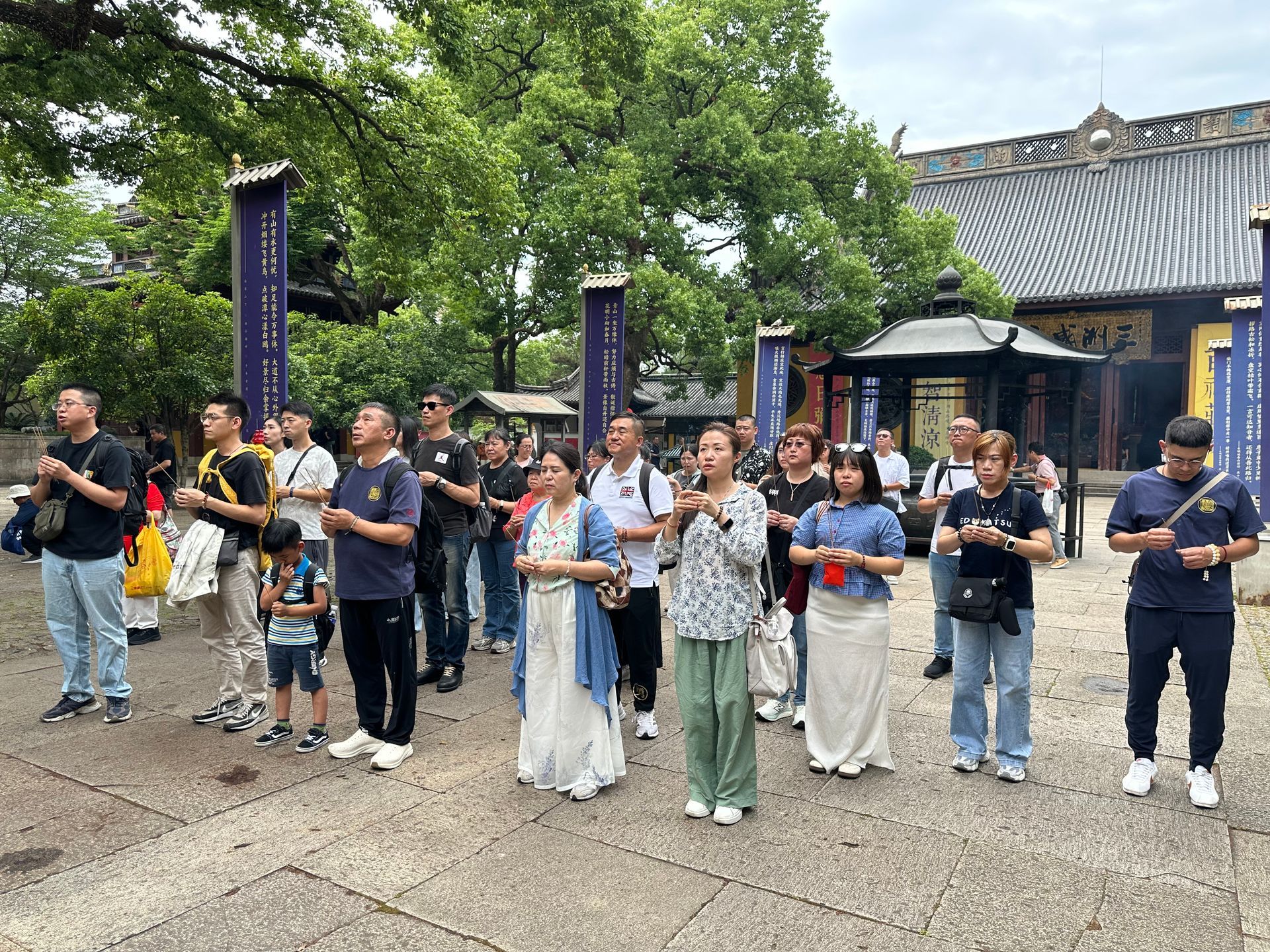 人們站在寺廟庭院裡，手裡拿著飲料，背景是樹木和亭台樓閣。