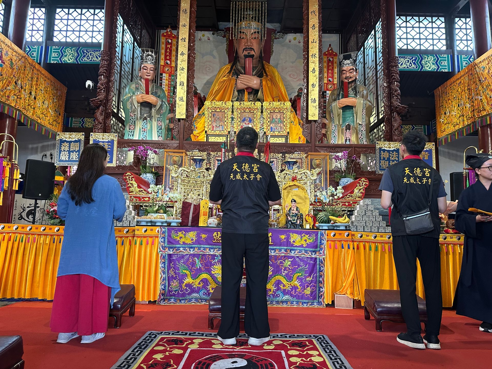 人們在寺廟大殿內，對著一座色彩繽紛、擺放著大型雕像的祭壇祈禱。