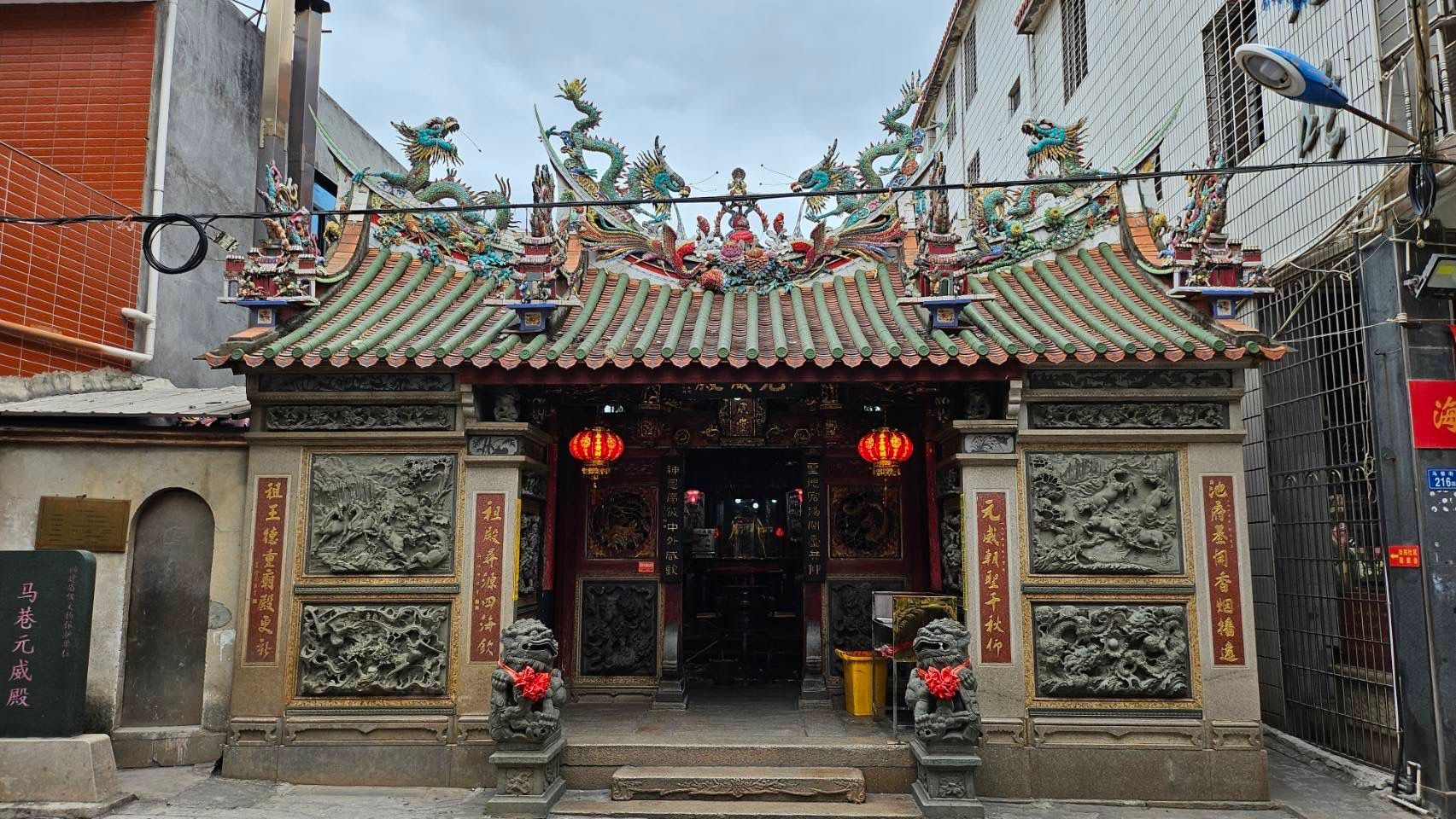 馬巷-元威殿池府王爺-裝飾精美的寺廟入口，屋頂華麗，掛著紅色燈籠，狹窄的街道上矗立著兩尊石獅。