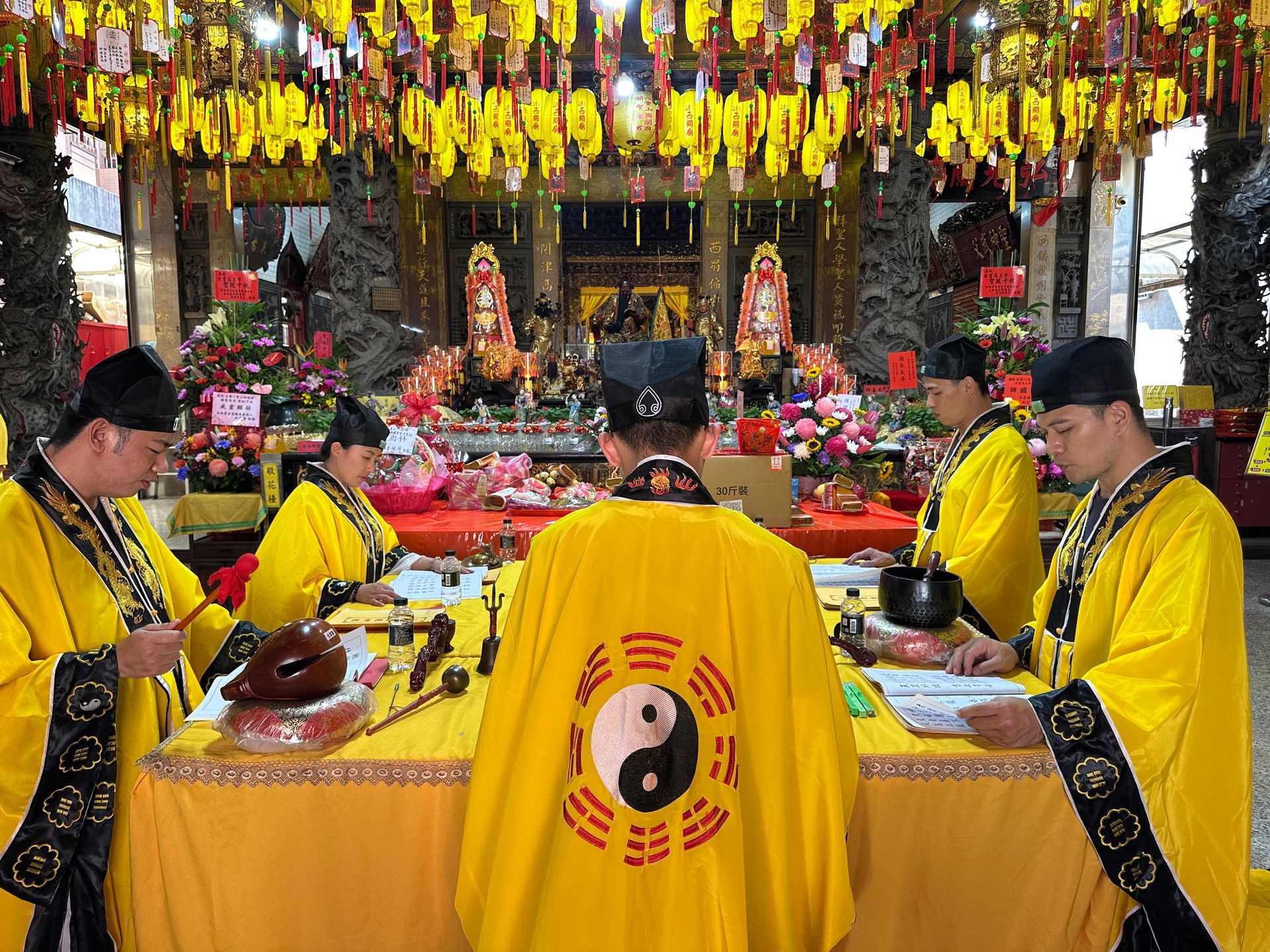 四名身穿黃色長袍的人在擺有祭品和紅色裝飾品的祭壇前舉行儀式。