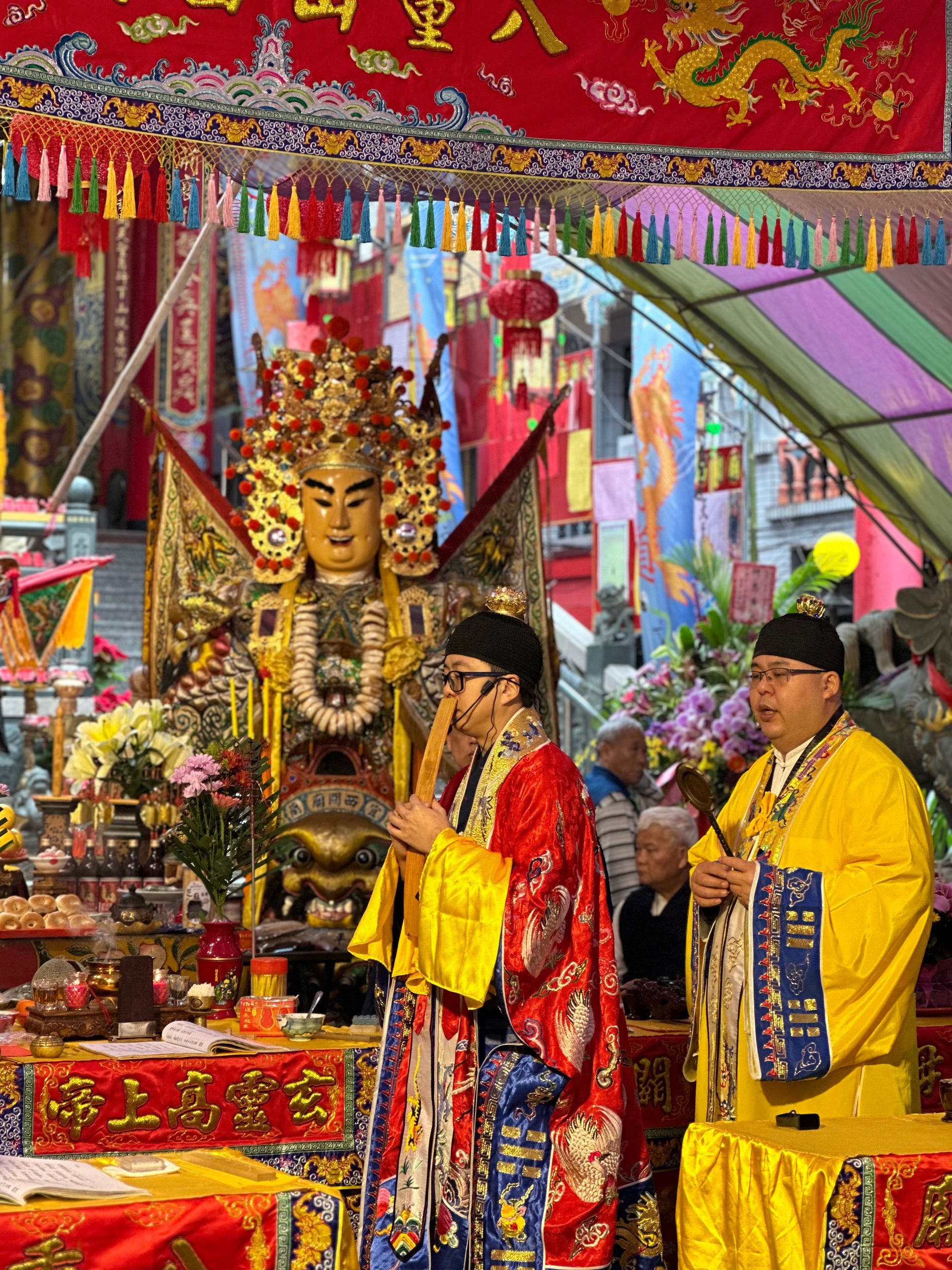 兩名身著華麗長袍的神像在色彩斑斕的寺廟祭壇前，祭壇上擺放著金色的神像和供品。