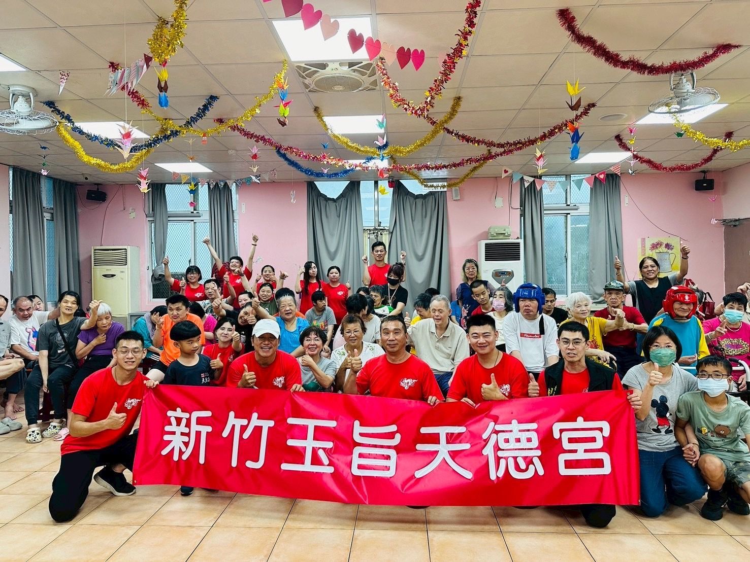 Group posing indoors with a red banner reading “新竹玉旨天德宮” and festive ceiling decorations.