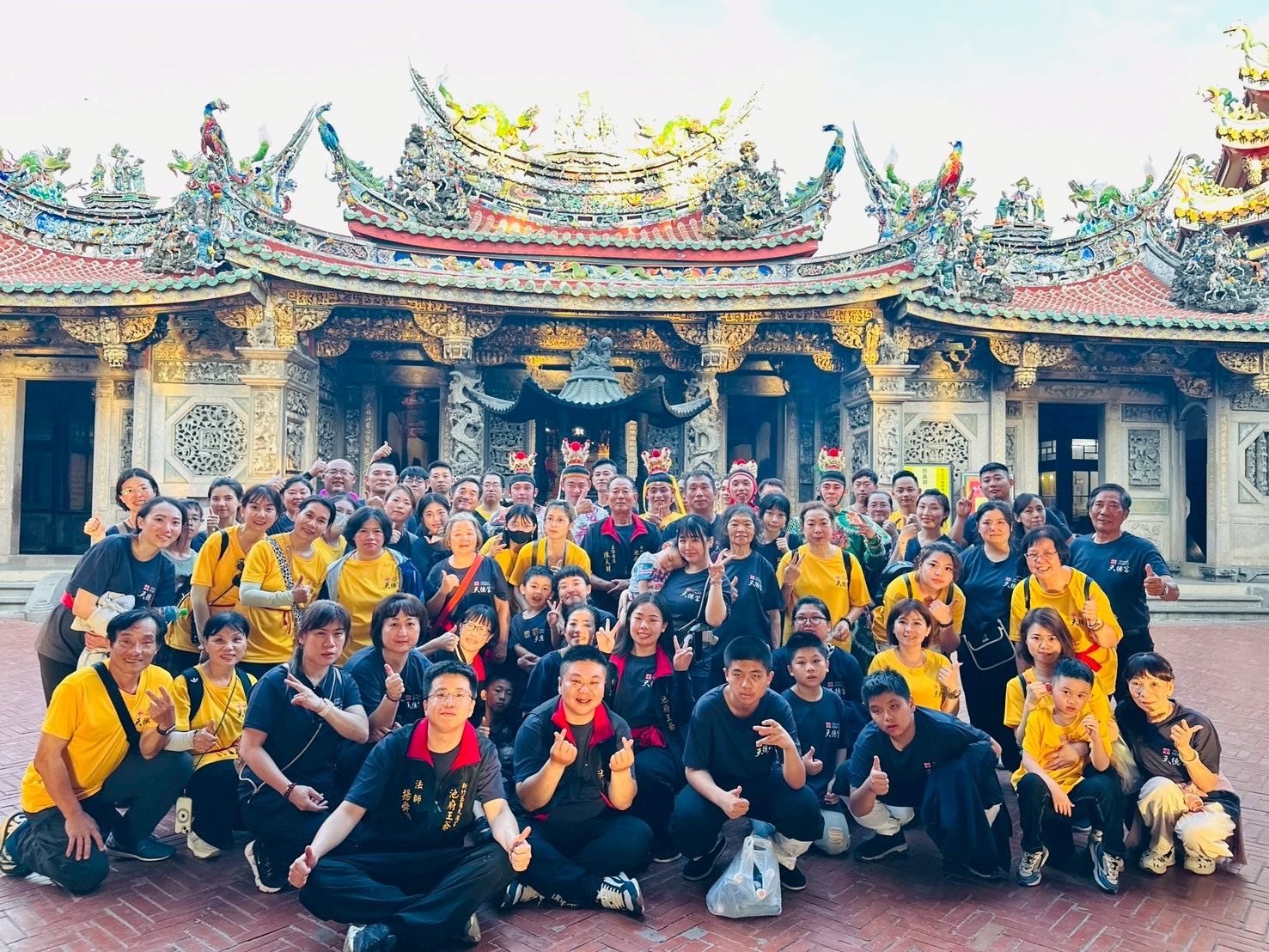 一大群人在一座裝飾華麗的寺廟前合影，許多人穿著黃黑相間的襯衫。