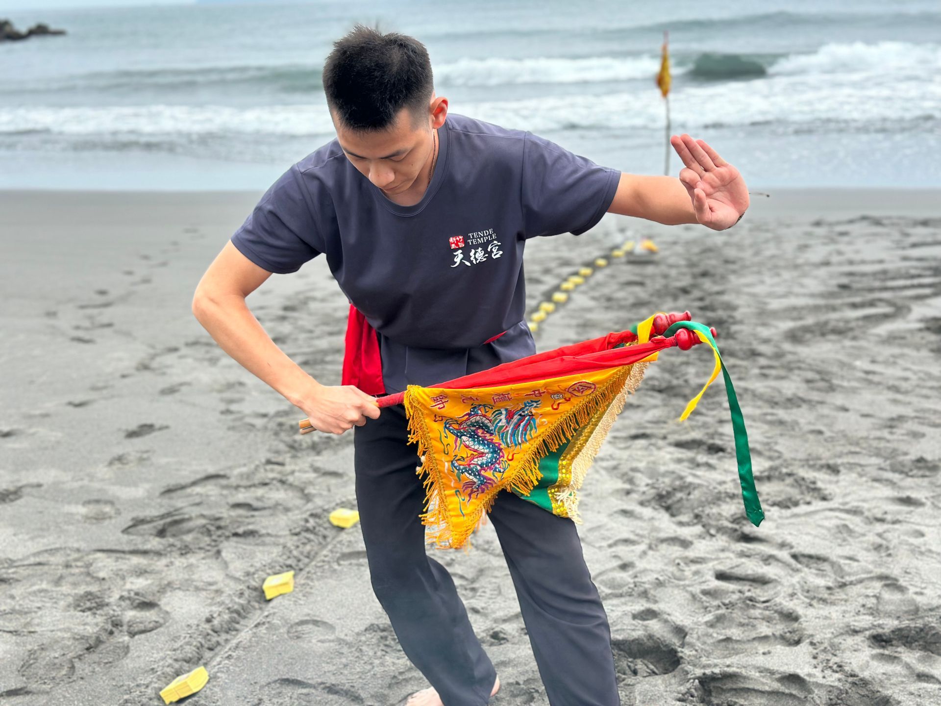 在海邊灰色的沙灘上，有人放飛著一隻色彩鮮豔的令旗。