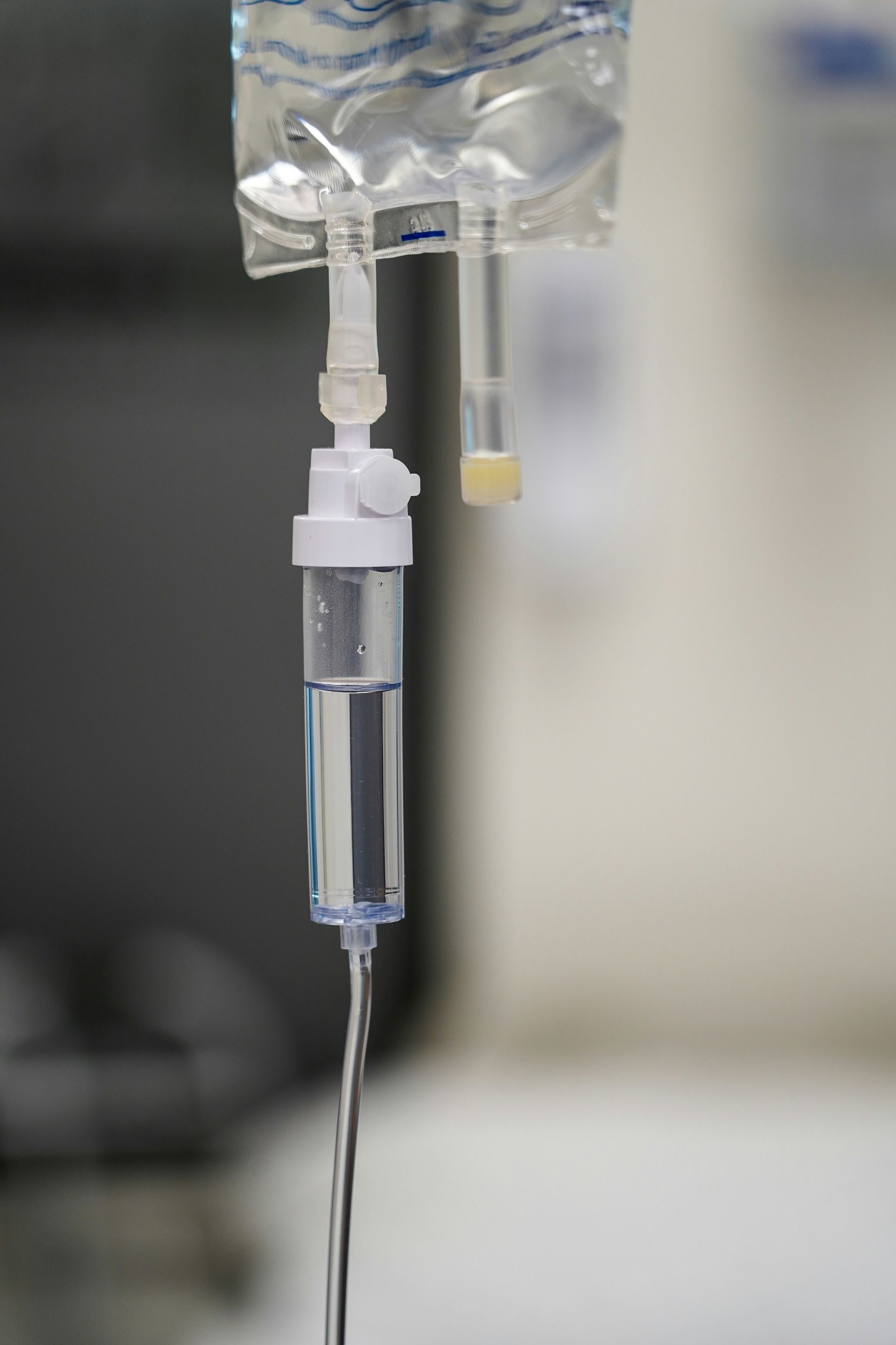 IV drip bag and tubing in a clinical setting; clear fluid drips from the bag.