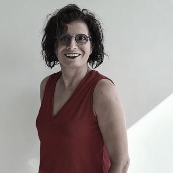 אישה עם משקפיים וגופייה אדומה מחייכת.