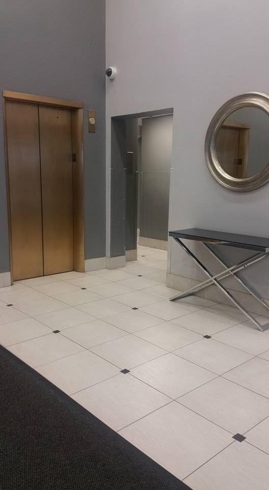Empty lobby with elevator doors, tiled floor, a round wall mirror, and an ironing board.