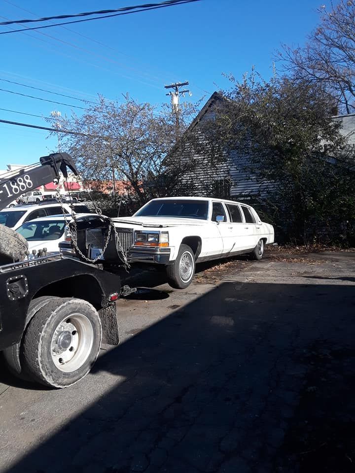 A white limousine is being towed by a tow truck.