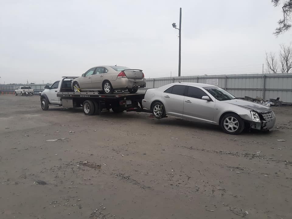 Two cars are being towed by a tow truck in a parking lot.