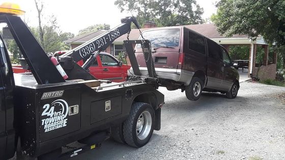 A tow truck is towing a van in a driveway.