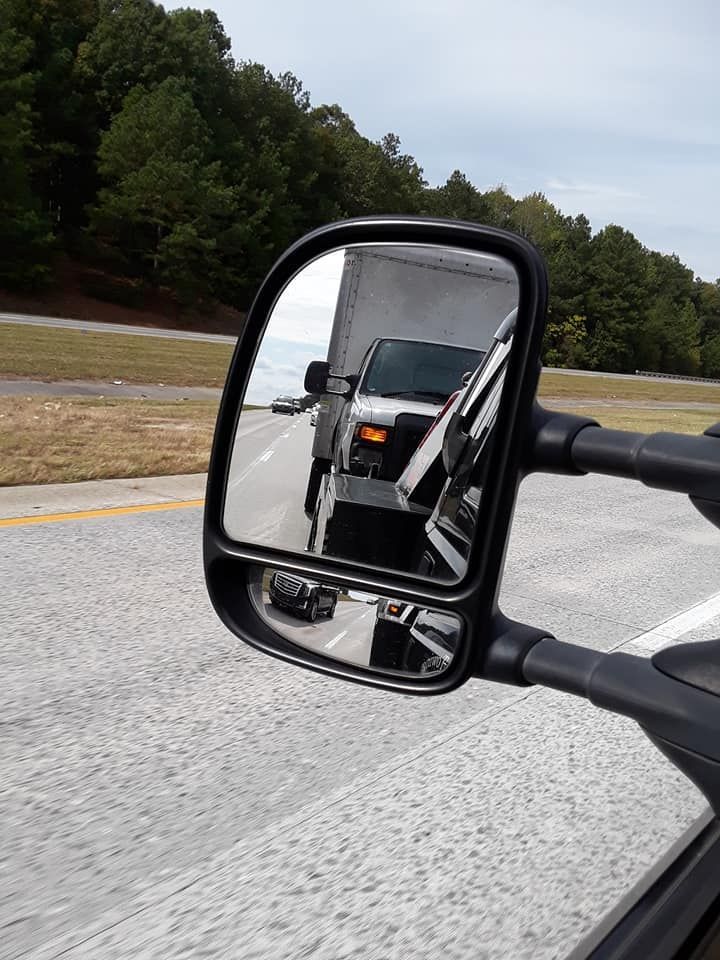 A truck is reflected in a side view mirror on a highway.
