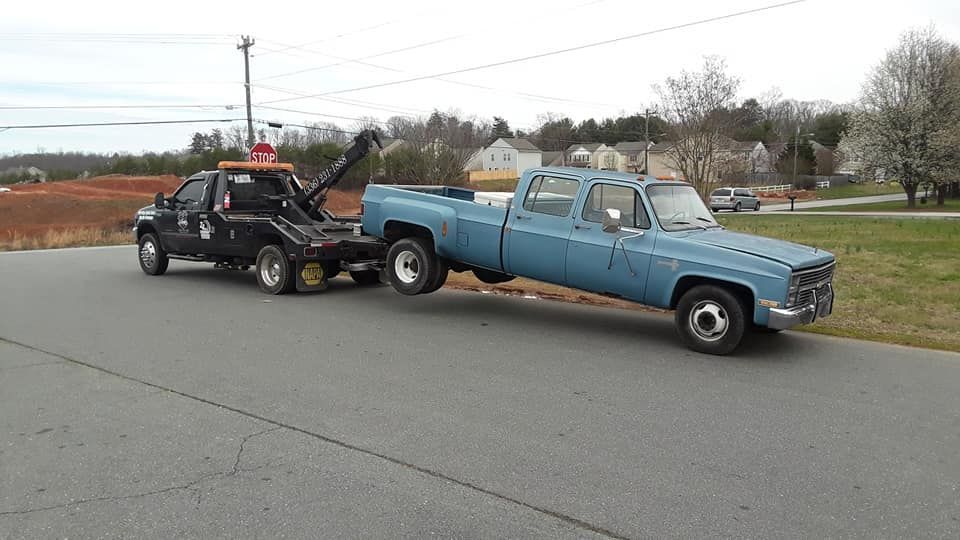 A blue truck is being towed by a black tow truck