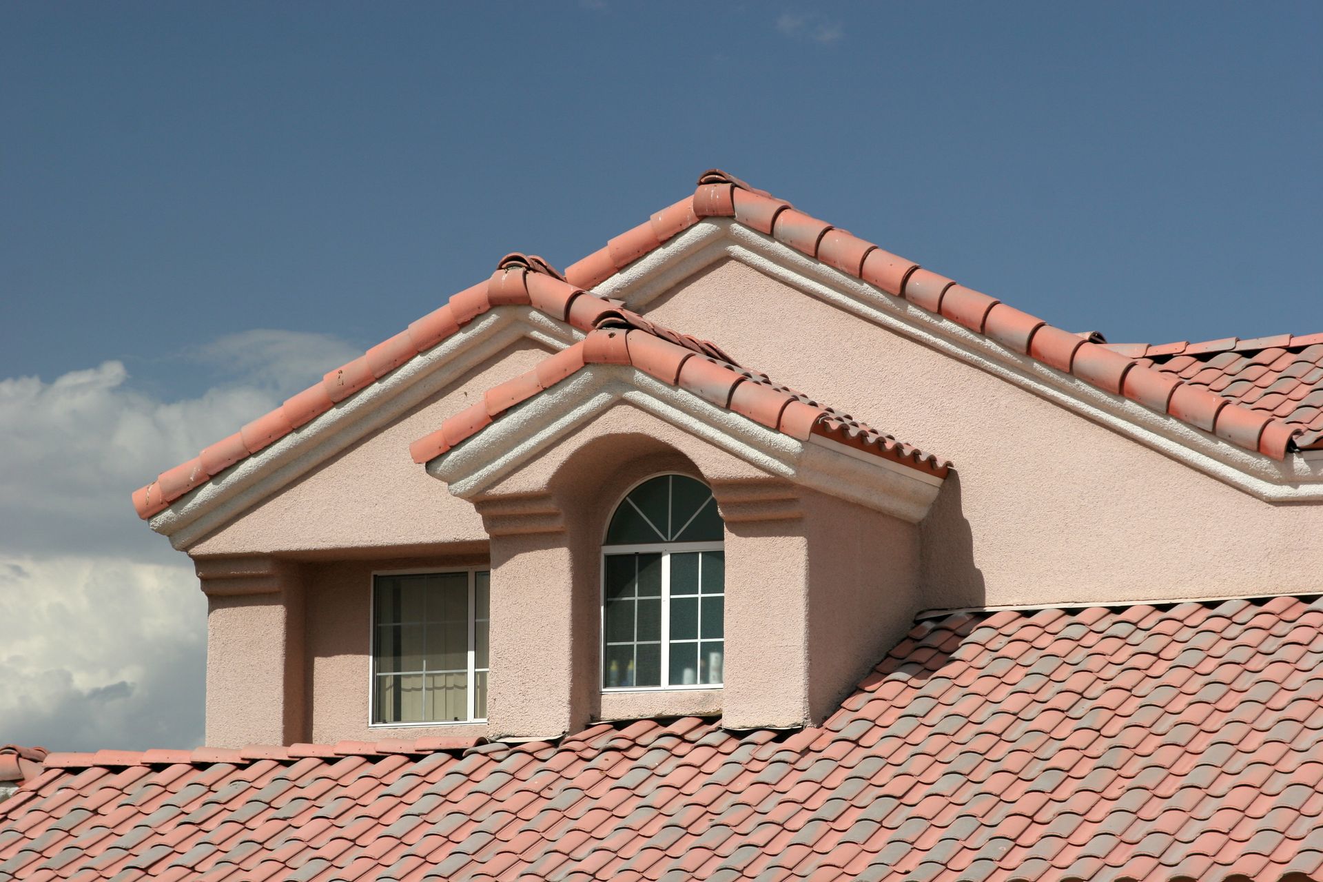 Red-tiled roof with a dormer window against a cloudy blue sky Red-tiled roof with a dormer window against a cloudy blue sky