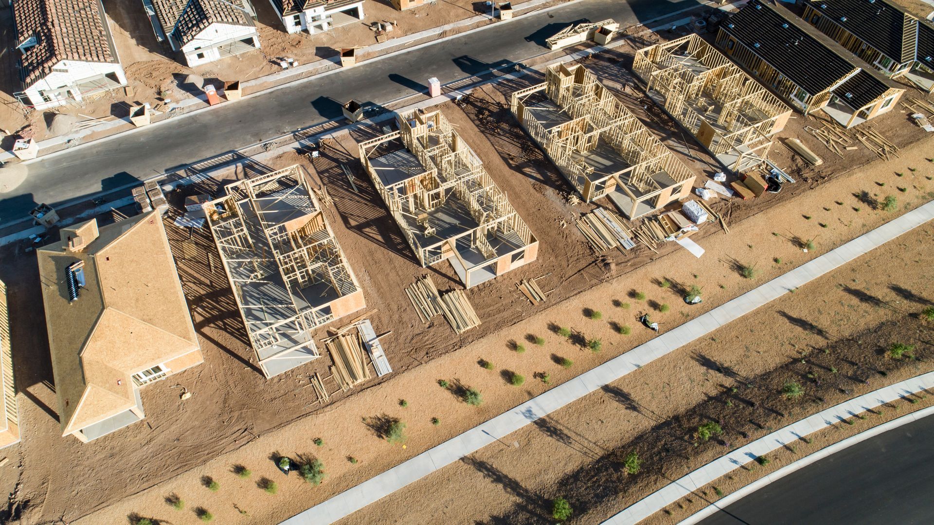 Aerial view of partially built homes in a desert neighborhood with roads and parked vehicles nearby Aerial view of partially built homes in a desert neighborhood with roads and parked vehicles nearby