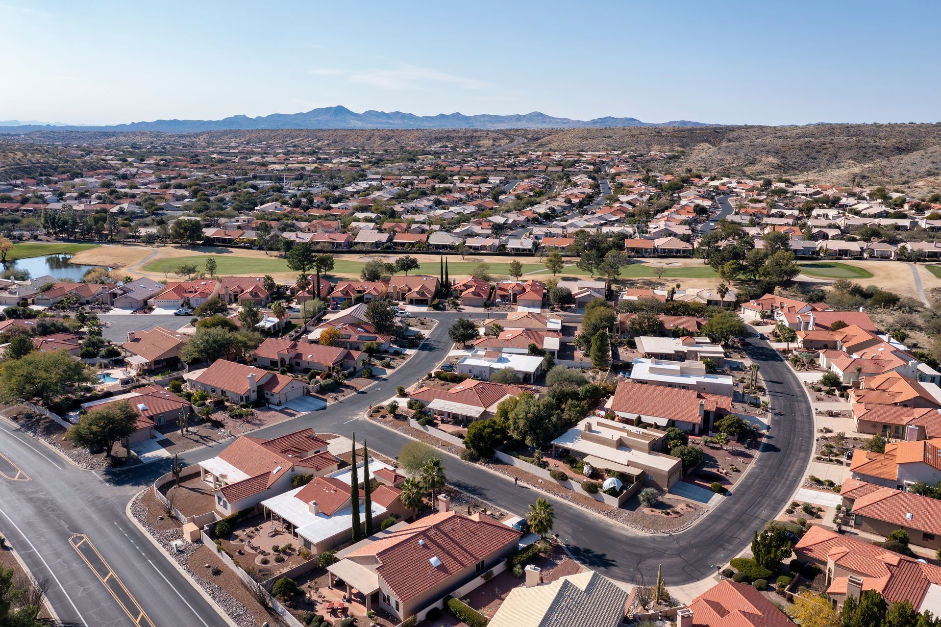 Aerial view of a suburban neighborhood with curving streets, red-roofed houses, and distant hills under a clear sky Aerial view of a suburban neighborhood with curving streets, red-roofed houses, and distant hills under a clear sky
