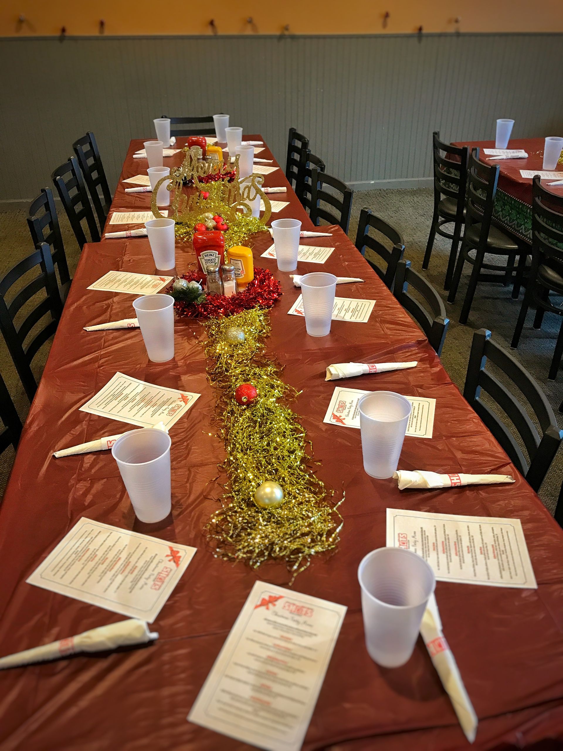 Long banquet table set with white cups, plates, and napkins, decorated with a gold and red centerpiece.